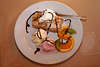 Eisdessert aus Apfelkuchen mit 2 Kugeln Eis in Bild mit Sahne, Kiwi, Orange-Scheibe garniert