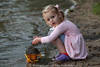 Kind blondes Mädchen mit Sandeimer Wasser Schlick am Seeufer
