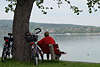 601618_ Paar Radler auf Bank unter Baum mit Fahrrder am Seeufer mit Bodensee Untersee Seeblick in Foto