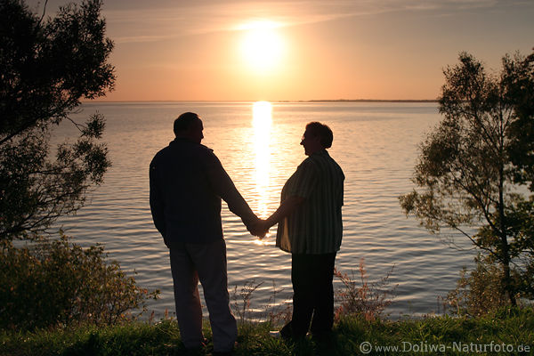 Senioren-Paar Mann Frau am Seeufer vor Sonne Gegenlicht