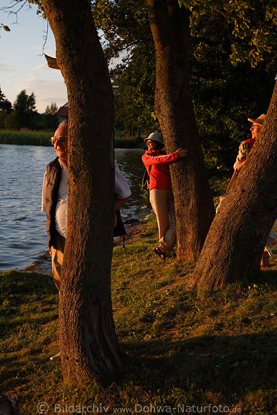 Trio hinter Baumstamm lustiges Fotoportrt am Seeufer jung-alt Romantik am Wasser