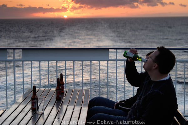 Mann trinkt Bier aus Flasche vor Sonnenuntergang ber Meerhorizont bei Schiffsreise