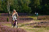 Fröhliches Mädel blond in Kleid lachen auf Fahrrad Fotos in Natur Lüneburger Heideblüte radeln