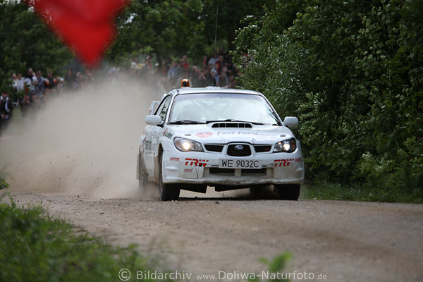 Subaru weisser Rennwagen spurt auf Schotterpiste vor Publikum Masuren-Rallye
