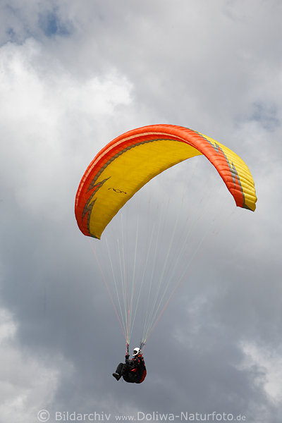 Gleitschirmflug Paragleiter unter Gelbschirm am Weisshimmel in Luft