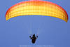 1202412_Gleitschirmvollbreite Flugfoto rot-gelb am Himmel in Blau über Pilot mit Leinen in Händen