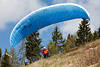 1201050_ Pilot breiten Gleitschirms in Blau am Berghang Startfoto Gleitsegelflieger vor Bäumen am Himmel