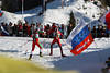 816325_ Biathleten Paar im Skilauf zwischen Fahnen der Zuschauer an Loipe im Biathlonstadion Foto