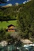 003285_Heuscheune Holzhäuschen Foto auf grüner Bergwiese über Bachwasser unter Waldbäumen am Hang Naturbild mit Wunspitze Gipfelsicht