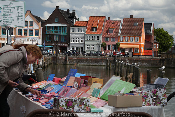 Husum Hafenflohmarkt Foto Trdelstand am Wasser Frau sucht Mitbringsel in Bild vor Friesenhusern