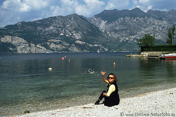 Fliegende Steine aus Mdchenhand wirft Kiessteine ber Gardasee-Strand Bergkulisse