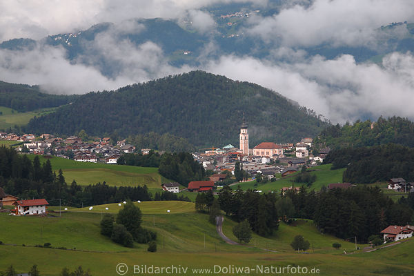 Blick auf Kastelruth Huser mit Kirche in grner Panorama Landschaft mit Wolkenschwaden