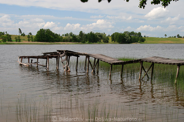 Schiefer Holzsteg in See Masuren Wasserlandschaft lustiges Frhling-Bild Ufer Panorama Mazury krzywa kladka wodna