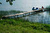 Seeufer-Steg mit Trettboot-Touristen liegen auf Holzsteg Schilf Wasserlandschaft Grünwiese Masuren Seeidylle