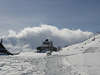 Sennhütte in Schneelandschaft am Skipfad Wanderpfad unter Wolke über Berg bei Wetterumschwung