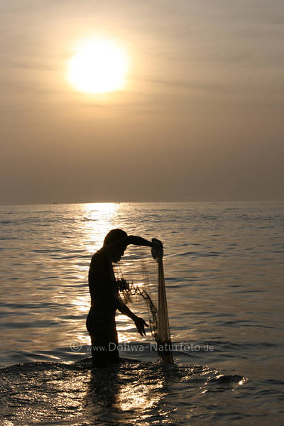 Thaifischer mit Wurfnetz im Wasser vor Sonne prft Fischnetz