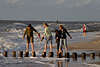 706014_ Mädchen Vierer Barfuss auf Wellenschutzpfahlen vor Gischt der Meerwellen am Seeufer, vier Mädels