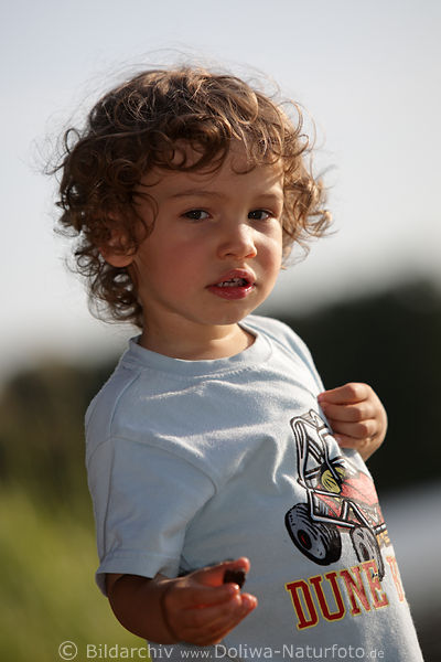 Junge Kind mit Stein in Hand Sprossling Gesicht mit Locken Nachwuchs Blick