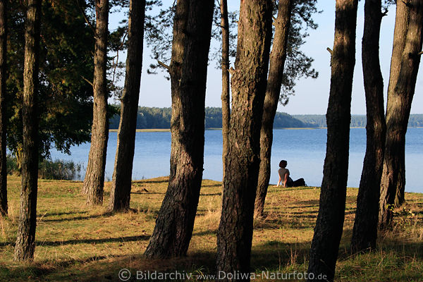 Baumufer-Frau am See Wasserblick unter Hochbumen sitzen relaxen