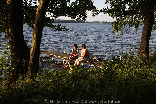 Frau-Paar auf Seesteg in Wasser Naturbild Girls unter Bumen sitzen