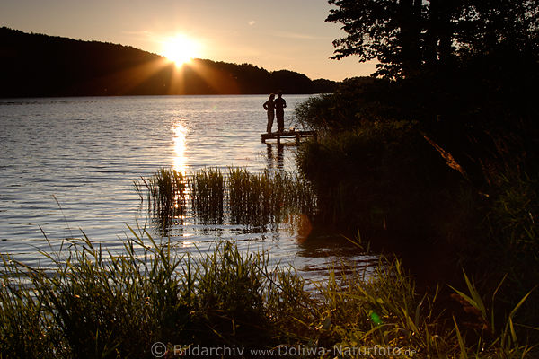 Paar am WasserSteg stehen vor Sonnenuntergang