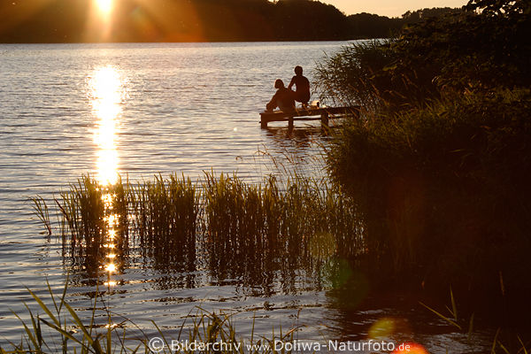 Paar Silhouetten am WasserSteg Foto in Abendsonne sitzen Romantiktreff in Sonnenstrahlen