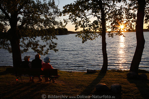 Trio auf Seeuferbank Freizeit-Relax vor Sonnenstern Romantik Sonnenuntergang ber Wasser