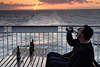 Mann trinkt Bier aus Flasche vor Sonnenuntergang über Meerhorizont bei Schiffsreise