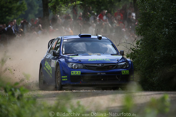 Subaru auf SchotterPiste Masuren Rally blauer Wagen Sprint Dynamik in Staub vor Fans in Kurve Mazury Rajd