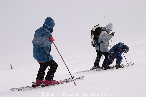 Skifamilien Skiurlaub in Schneetreiben Skifahrer auf Skipiste skifahren mit Kind Nachwuchs
