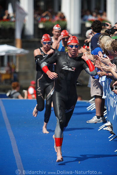 Triathlet Russe Denis Vasiliev auf Blauteppich am Publikumspalier laufen im schwarzen Schwimmanzug