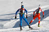 Biathleten Paar bei Skilauf auf schneeweissen Loipe mit Gewehren im Lauf auf Biathlonstrecke